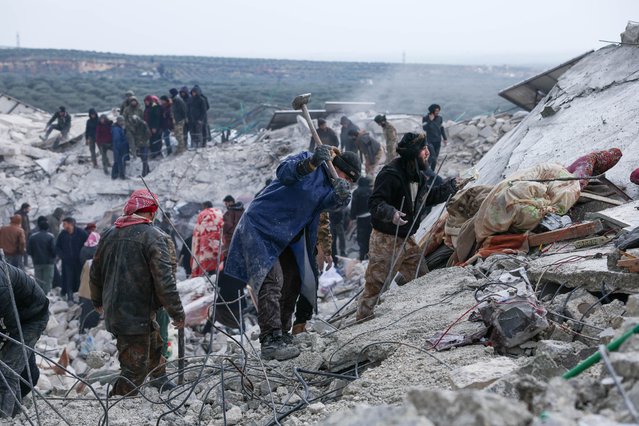 Een man met een bijl hakt in op een het puin van de aardbeving in Syrië en Turkije. Om hem heen loopt een groep mannen rond die door het puin zoeken.