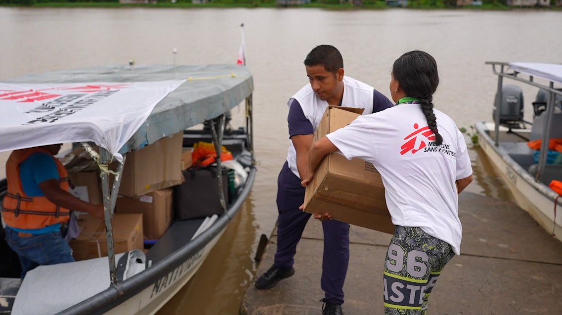Twee personen in een Artsen zonder Grenzen t-shirt laden een grote doos op een bootje vanaf een steiger.