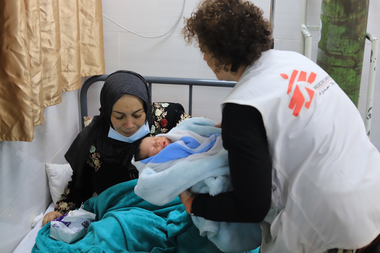 Een verloskundige met een wit vestje met Artsen zonder Grenzen logo overhandigd een kleine in een deken gewikkelde baby aan de moeder