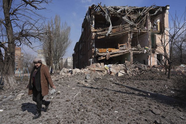 Een vrouw loopt langs een gebouw dat geraakt is door beschietingen. Mariupol, Oekraïne,13 maart 2022. © Evgeniy Maloletka/AP Photo