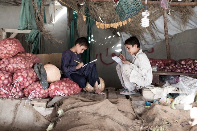 Kinderen maken hun huiswerk in een fruitstalletje op een markt in Afghanistan