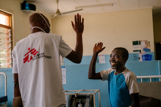 Twee mannen geven elkaar een high five. De linker man draagt een shirt van Artsen zonder Grenzen en de rechter man zit op een ziekenhuisbed en lacht.