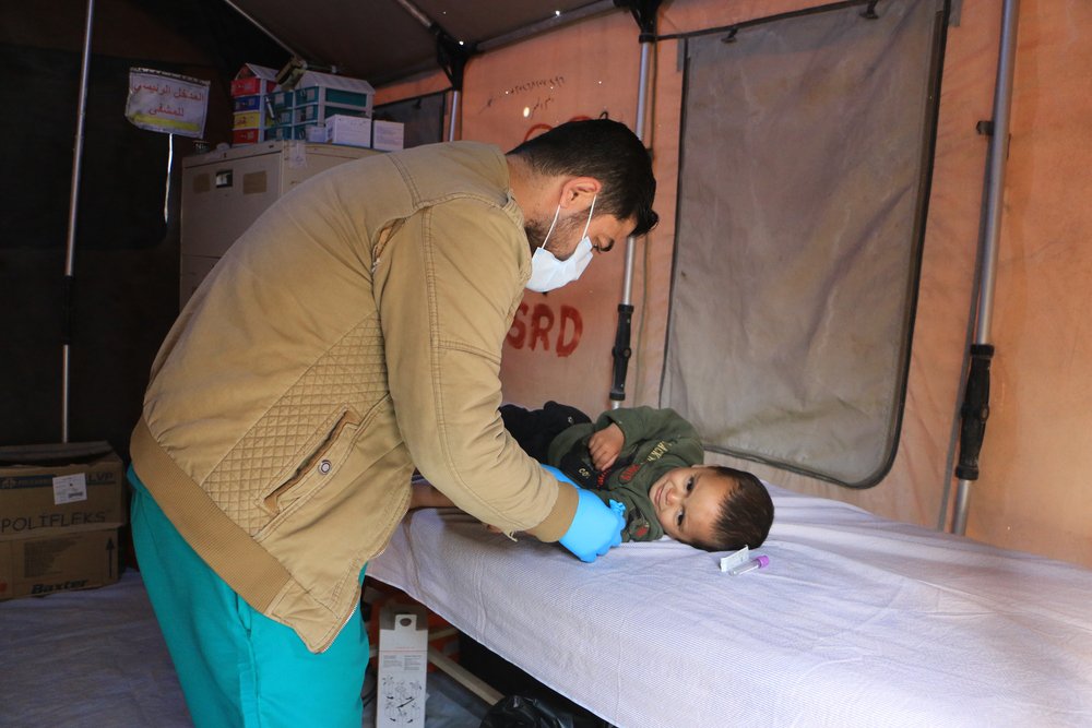 Een klein kindje op een bed in een medische tent wordt onderzocht door een arts.
