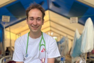 kinderarts Michael Malley zit met een grote lach op zijn gezicht op een tafel in een medische tent van artsen zonder granzen