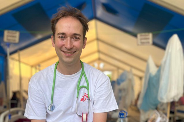 kinderarts Michael Malley zit met een grote lach op zijn gezicht op een tafel in een medische tent van artsen zonder granzen