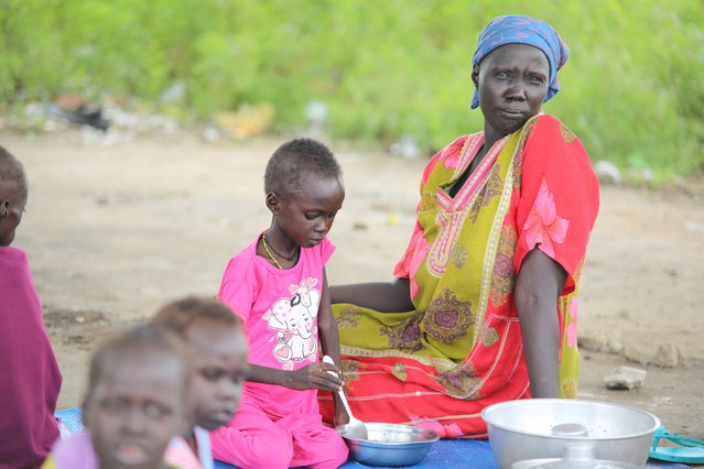 Een vrouw genaamd Marta Kalibe zit in kleurrijke kleding op een kleed naast haar dochter die met een lepel in een kom roert.