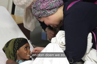 Kind ligt op bed en moeder leunt voorover naar kind in veldhospitaal in Jemen