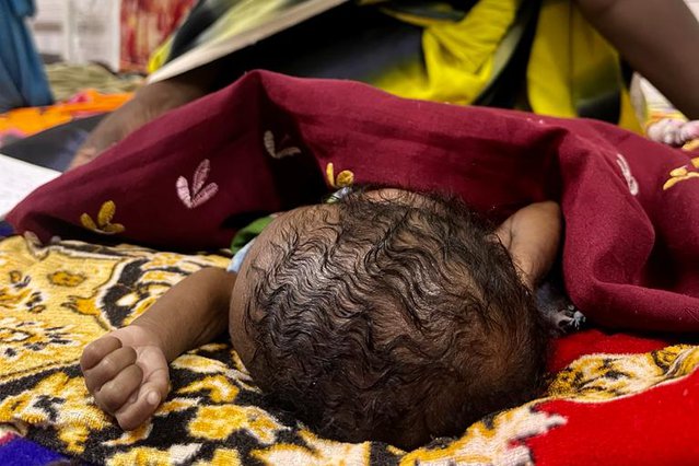 Een kleine te vroeg geboren baby ligt te slapen onder een deken. Haar moeder zit achter haar kindje.