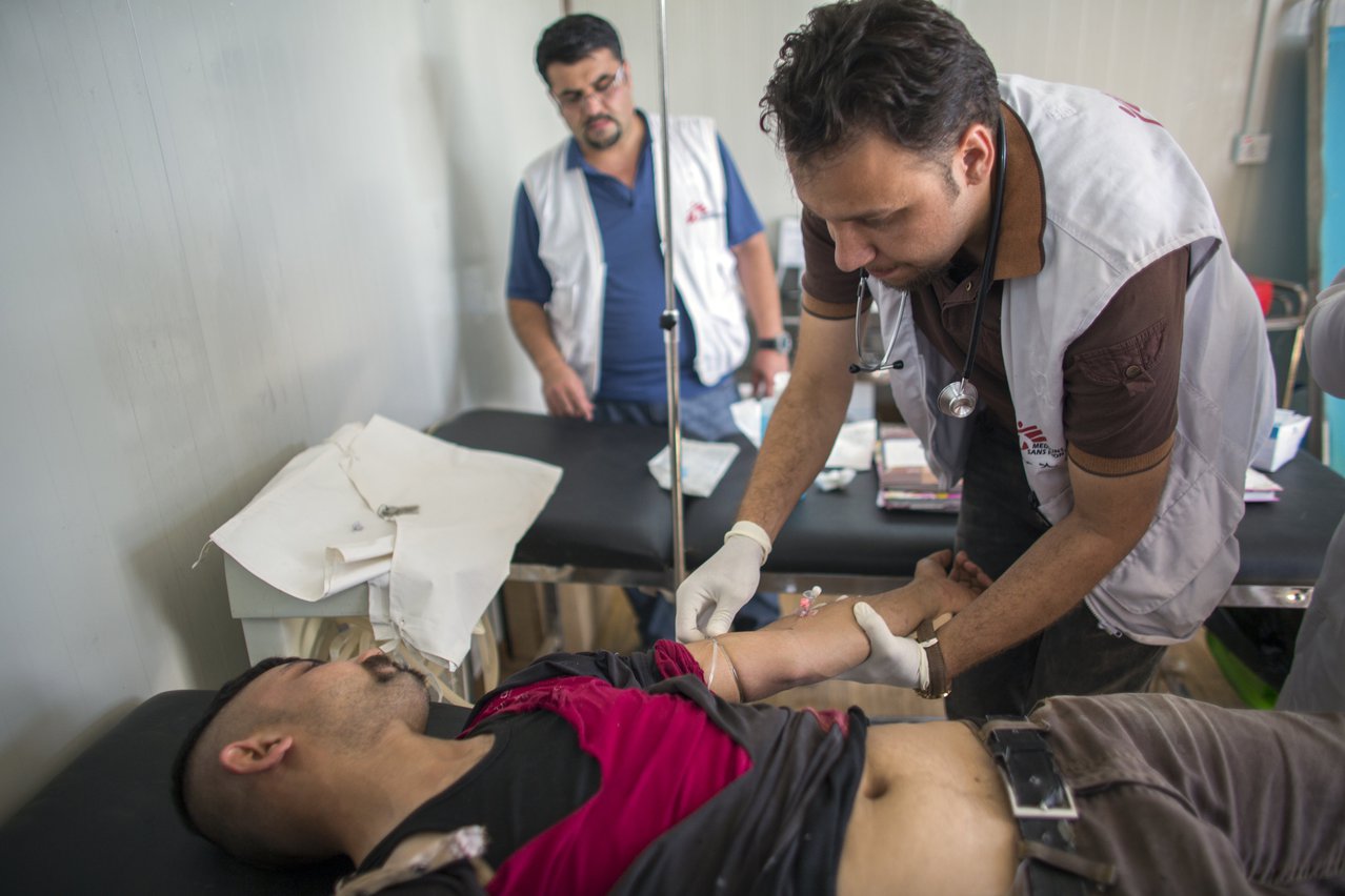 Arts behandelt een Irakese vluchteling die als arbeider werk verrichtte op een container in het kamp